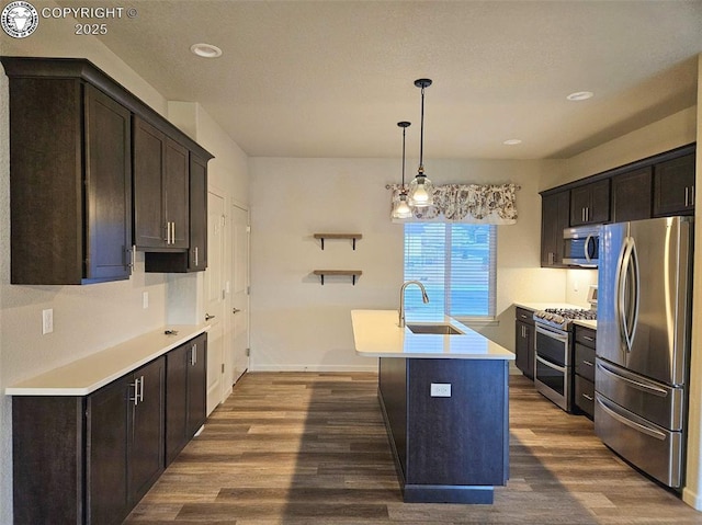 kitchen with an island with sink, sink, dark hardwood / wood-style flooring, stainless steel appliances, and dark brown cabinets