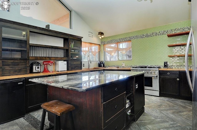 kitchen featuring open shelves, lofted ceiling, dark cabinetry, and stainless steel range