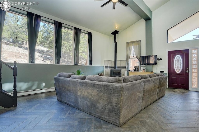 living room featuring a baseboard heating unit, a wood stove, ceiling fan, and high vaulted ceiling