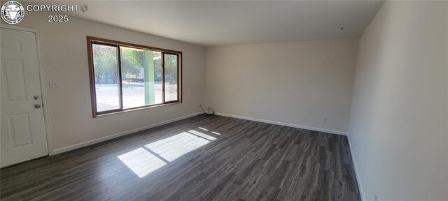 unfurnished room with baseboards, visible vents, and dark wood-style floors