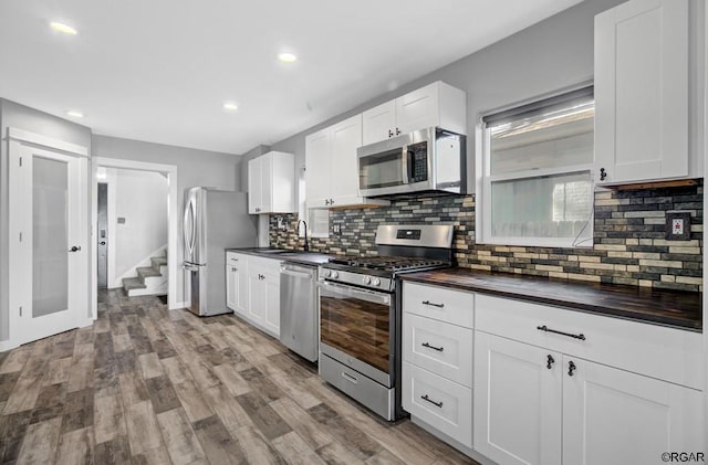 kitchen featuring sink, backsplash, white cabinets, stainless steel appliances, and light wood-type flooring