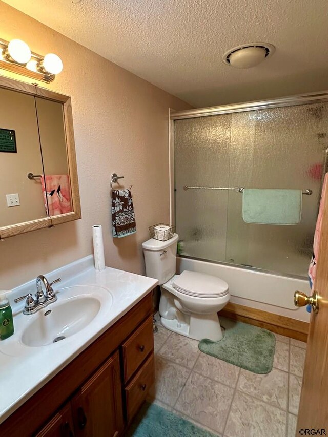 full bathroom with bath / shower combo with glass door, vanity, a textured ceiling, and toilet