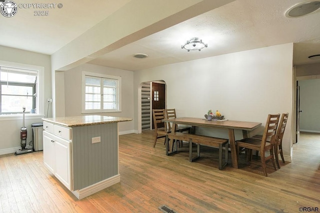 kitchen with white cabinetry, light stone counters, a kitchen island, and light wood-type flooring