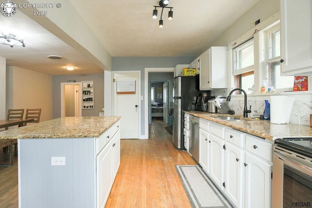 kitchen with appliances with stainless steel finishes, sink, white cabinets, a center island, and light hardwood / wood-style floors