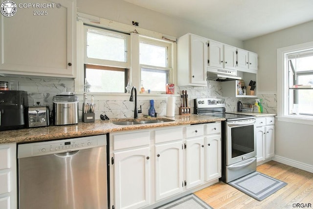 kitchen with appliances with stainless steel finishes, white cabinetry, sink, light hardwood / wood-style floors, and light stone countertops