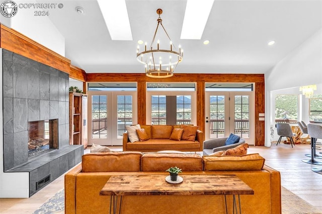 living room with light hardwood / wood-style flooring, an inviting chandelier, a fireplace, a healthy amount of sunlight, and french doors