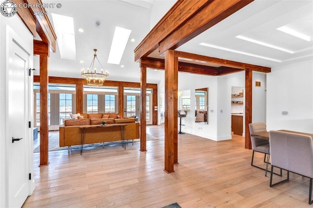 interior space featuring a notable chandelier, beam ceiling, a skylight, and light wood-type flooring