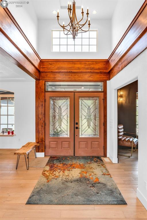 entrance foyer featuring a towering ceiling, light hardwood / wood-style flooring, french doors, and a chandelier