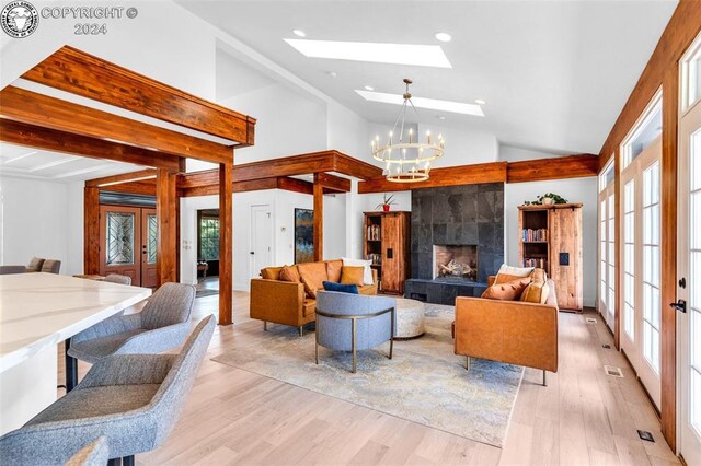 living room featuring an inviting chandelier, a skylight, high vaulted ceiling, a tiled fireplace, and light hardwood / wood-style floors