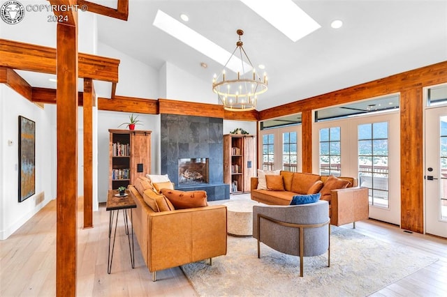 living room with an inviting chandelier, a tile fireplace, vaulted ceiling with skylight, and light hardwood / wood-style floors