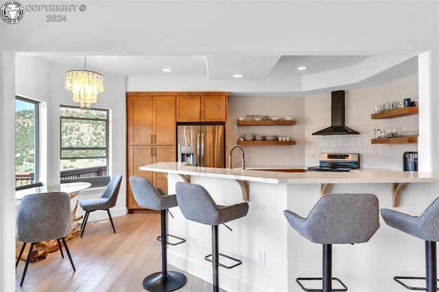 kitchen featuring wall chimney exhaust hood, a breakfast bar, hanging light fixtures, appliances with stainless steel finishes, and decorative backsplash