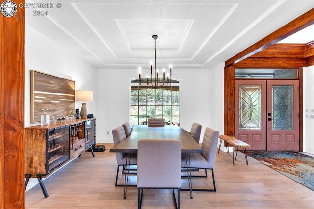 dining space with french doors, a notable chandelier, a tray ceiling, and light wood-type flooring