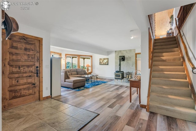 foyer entrance with a wood stove, light wood-style flooring, stairs, and baseboards