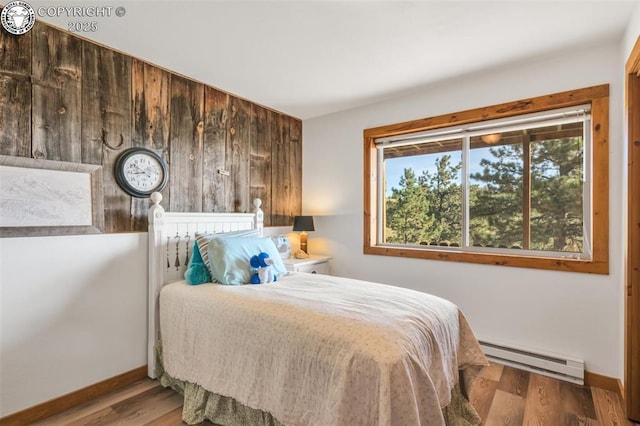 bedroom with wooden walls, baseboards, baseboard heating, and wood finished floors