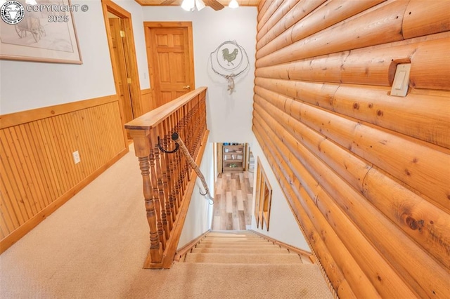 hallway featuring wainscoting, rustic walls, carpet, and an upstairs landing