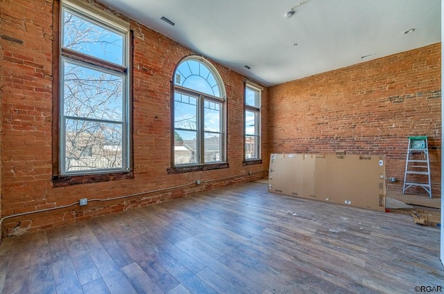 empty room with hardwood / wood-style flooring, brick wall, and a towering ceiling