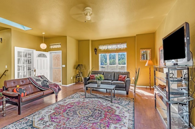 living room featuring ceiling fan, wood-type flooring, and a skylight