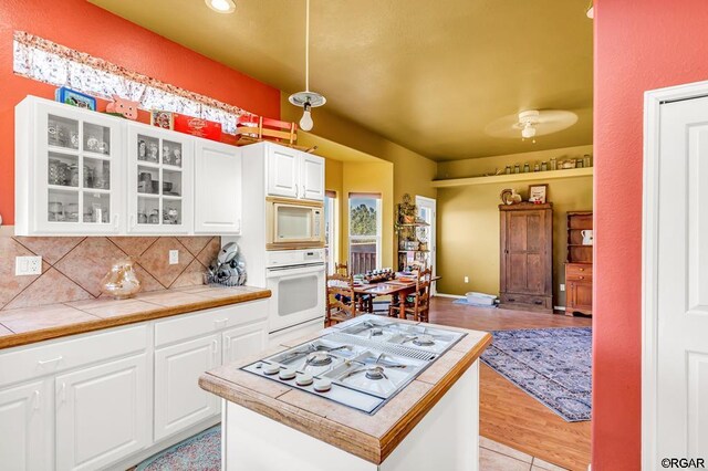 kitchen featuring white appliances, white cabinetry, hanging light fixtures, tile counters, and decorative backsplash