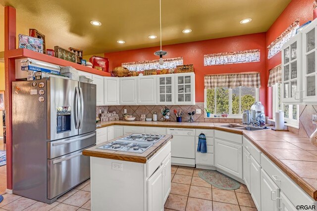 kitchen featuring light tile patterned flooring, tile countertops, white cabinets, a center island, and stainless steel appliances