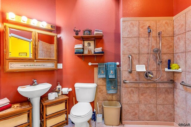 bathroom featuring tiled shower, sink, and toilet