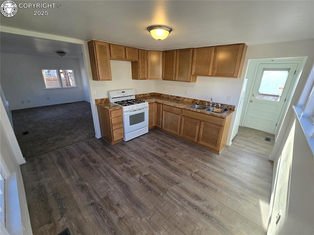 kitchen with sink, dark wood-type flooring, dark stone counters, and white range with gas stovetop