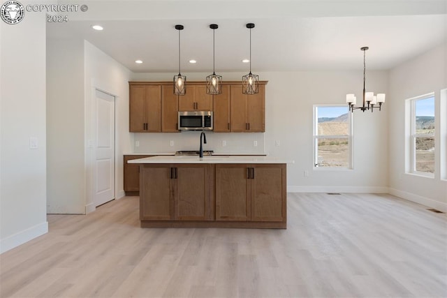 kitchen with decorative light fixtures, stove, a notable chandelier, a center island with sink, and light hardwood / wood-style flooring