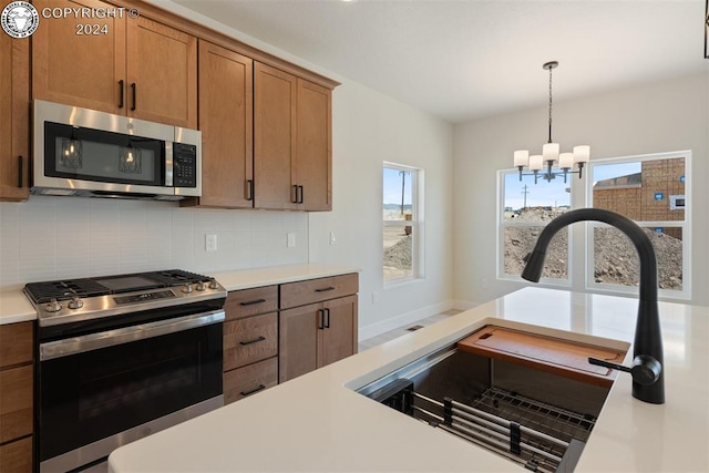 kitchen with sink, appliances with stainless steel finishes, an inviting chandelier, decorative backsplash, and decorative light fixtures