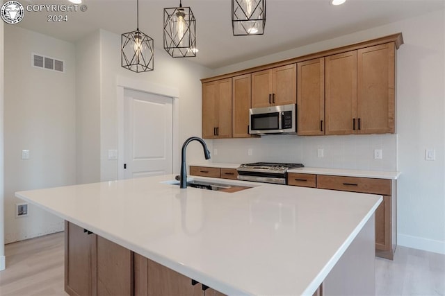 kitchen with stainless steel appliances, hanging light fixtures, a kitchen island with sink, and sink