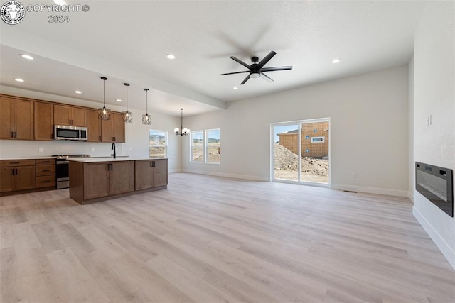 kitchen with sink, a kitchen island with sink, stainless steel appliances, decorative light fixtures, and light wood-type flooring