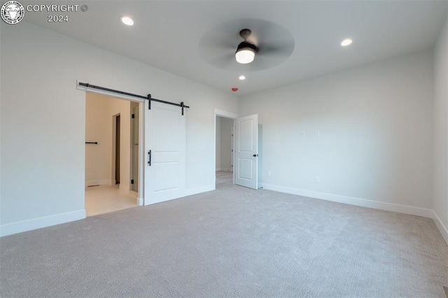 unfurnished bedroom with ensuite bathroom, a barn door, light colored carpet, and ceiling fan