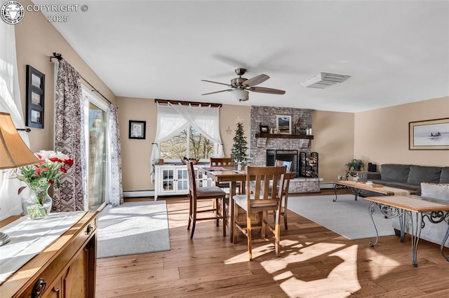 dining room with ceiling fan, a fireplace, light hardwood / wood-style floors, and a baseboard heating unit