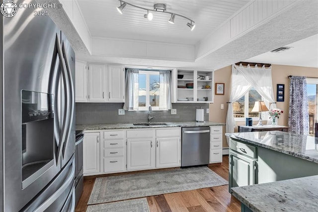 kitchen with sink, white cabinetry, wood-type flooring, stainless steel appliances, and light stone countertops