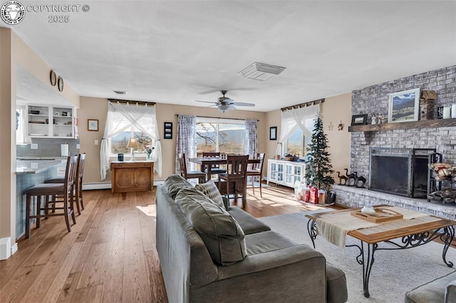 living room featuring a baseboard radiator, light wood-type flooring, ceiling fan, and a fireplace