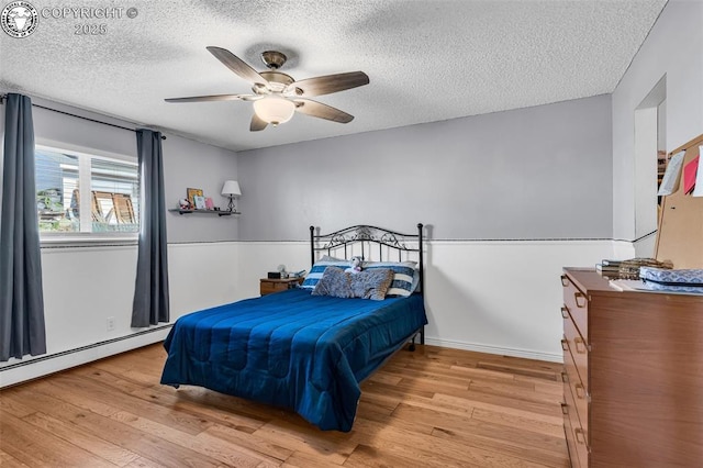 bedroom with a textured ceiling, light hardwood / wood-style floors, ceiling fan, and baseboard heating