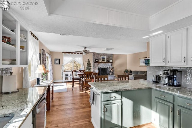 kitchen featuring light stone counters, light hardwood / wood-style flooring, ceiling fan, a fireplace, and white cabinets