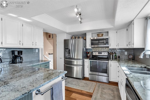 kitchen with sink, appliances with stainless steel finishes, light stone countertops, white cabinets, and a raised ceiling