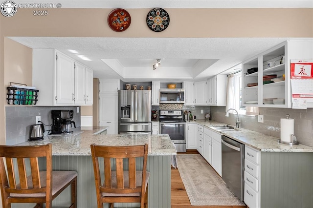 kitchen featuring sink, white cabinetry, appliances with stainless steel finishes, a raised ceiling, and light stone countertops