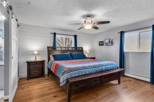 bedroom with baseboard heating, ceiling fan, multiple windows, and light wood-type flooring