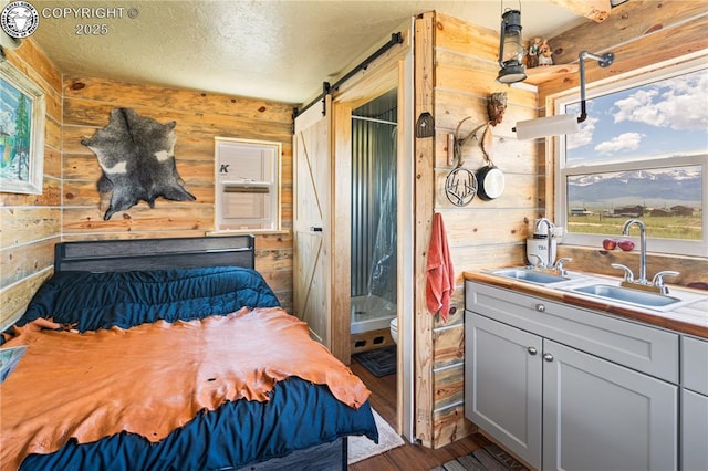 bedroom with sink, a barn door, hardwood / wood-style floors, and wood walls