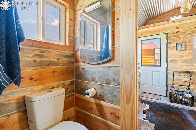 bathroom featuring vaulted ceiling, wooden walls, and toilet