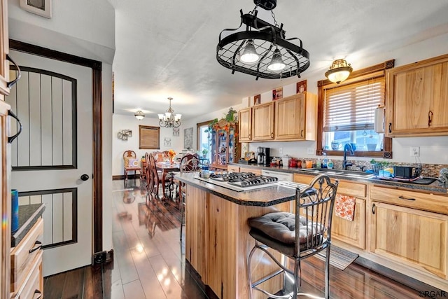 kitchen with a kitchen bar, stainless steel gas cooktop, sink, a kitchen island, and pendant lighting