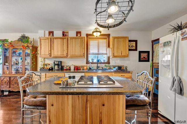 kitchen with a breakfast bar, sink, a center island, white fridge with ice dispenser, and stainless steel gas stovetop