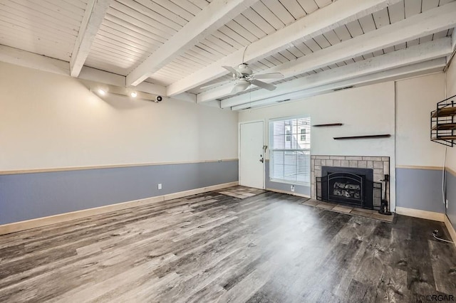 unfurnished living room with dark wood-type flooring, ceiling fan, a tiled fireplace, and beamed ceiling