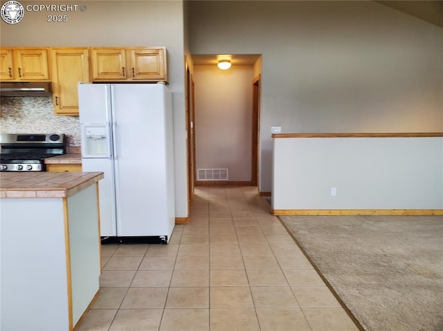 kitchen with light brown cabinets, visible vents, stove, under cabinet range hood, and white fridge with ice dispenser