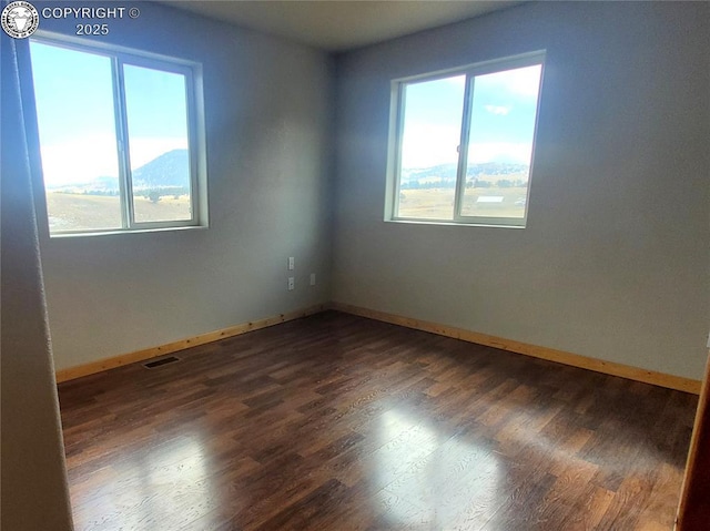 empty room with baseboards, a mountain view, visible vents, and dark wood finished floors