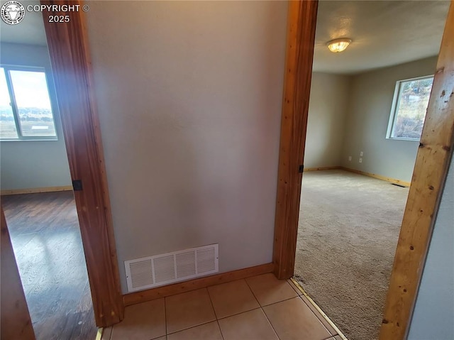 corridor with light tile patterned floors, plenty of natural light, visible vents, and light colored carpet