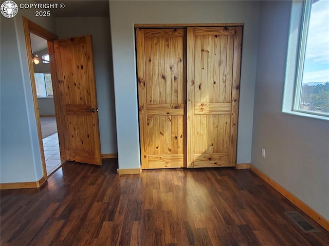 unfurnished bedroom featuring dark wood-style floors, visible vents, and baseboards