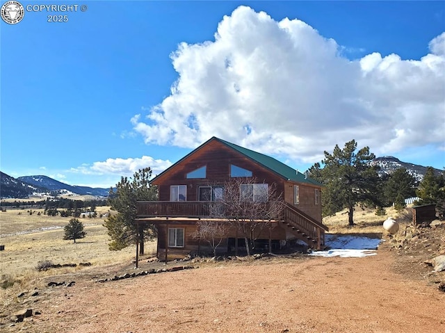 rear view of property featuring stairs, a deck with mountain view, and a rural view