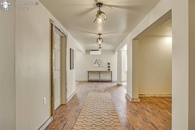 hallway with an AC wall unit, baseboards, and wood finished floors