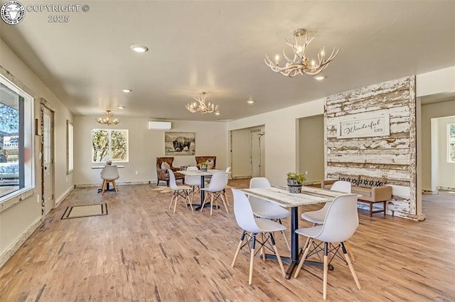 dining area with light wood-type flooring, an AC wall unit, and an inviting chandelier